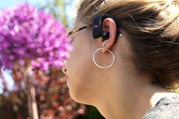Frau hat Soundcore Headset im Ohr und sitzt vor einer lila Blume