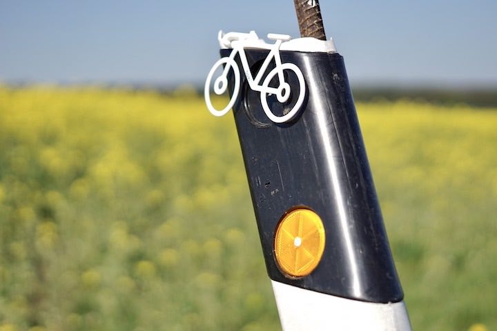 Baiki Gummi Fahrrad Halterung haengt an einem Leitpfosten vor einem gelben Feld