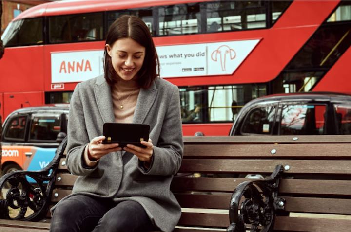 Frau sitzt auf Bank vor Bus und hat Astro Slide 5G Transformer in der Hand