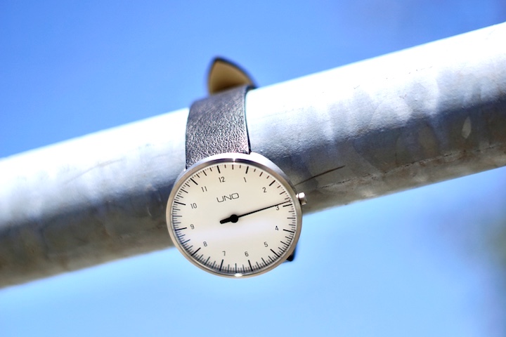 BOTTA Design Uhr Uno haengt an einer Metallstange vor blauem Himmel