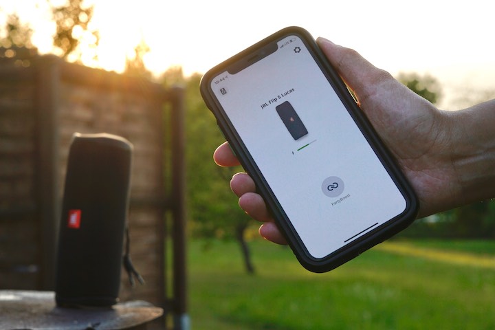 JBL Connect App auf iPhone vor einem kabellosen Lautsprecher in der Sonne