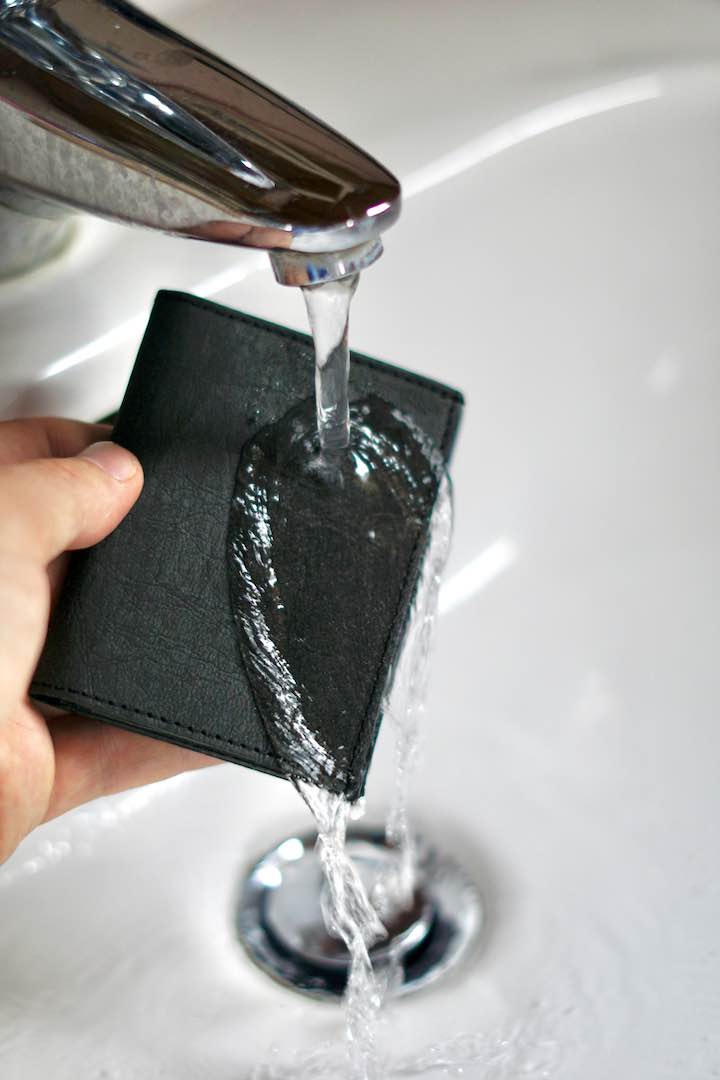 Hand waescht Tiny Wallet unter einem Wasserhahn ab