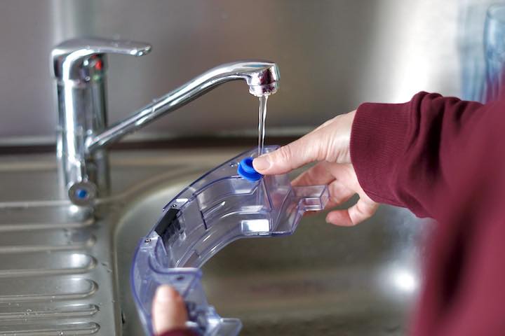 Haende halten Wassertank fest der gerade gefuellt wird