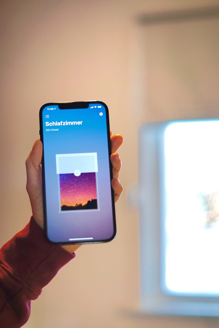 Smart Shades App auf einem iPhone mit Fenster im Hintergrund