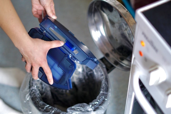 Haende leeren Staubtank ueber einem Muelleimer aus