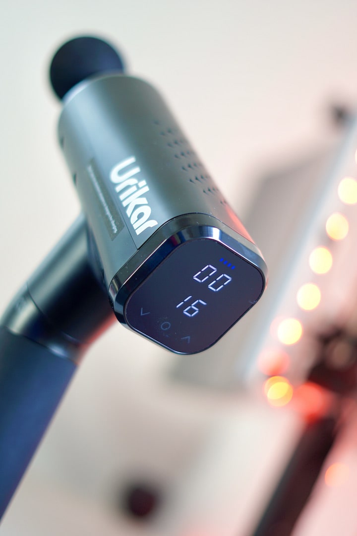 Urikar Pro 3 Massage Gun mit Display und Bokeh im Hintergrund