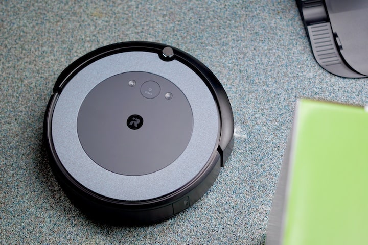 iRoomba Saugroboter auf Teppich neben gruener Verpackung