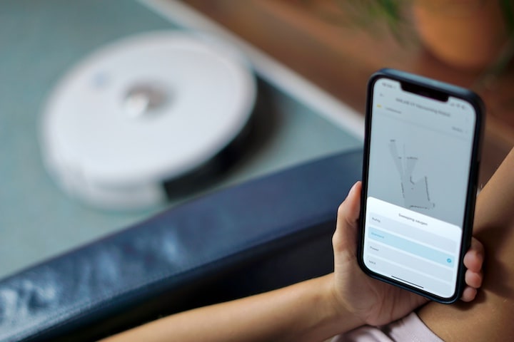 Hand mit iPhone steuert Saugroboter mit einer App