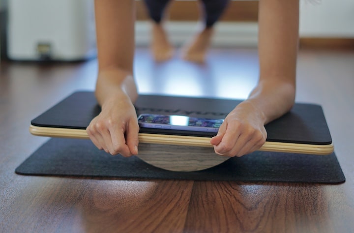 Frau balanciert mit den Armen auf einem Plankpad PRO