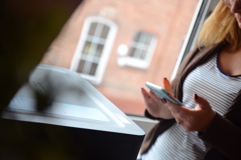 Frau mit Handy neben Drucker