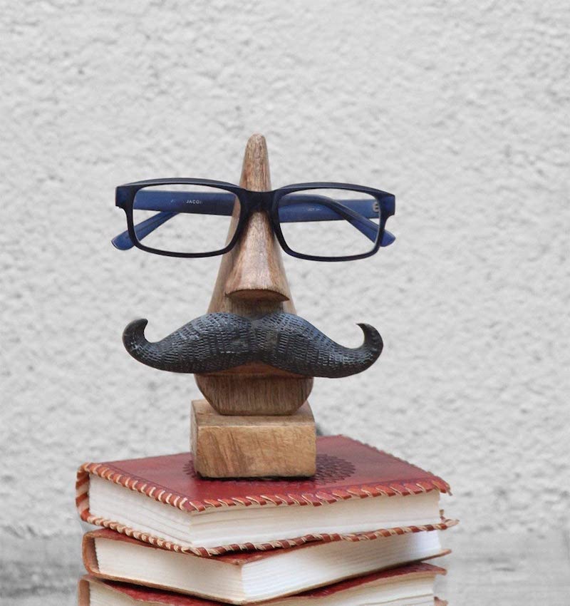 Brillenhalter aus Holz mit Schnauzer steht auf Buchstapel