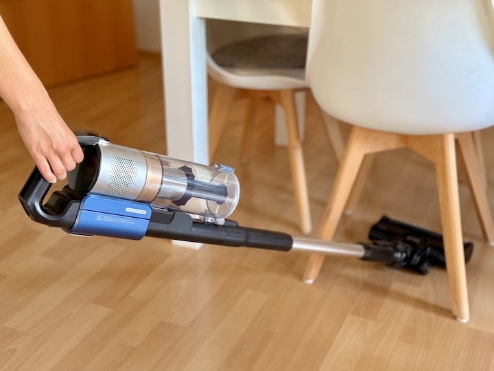 Hand mit Sauger reinigt unter einem Tisch